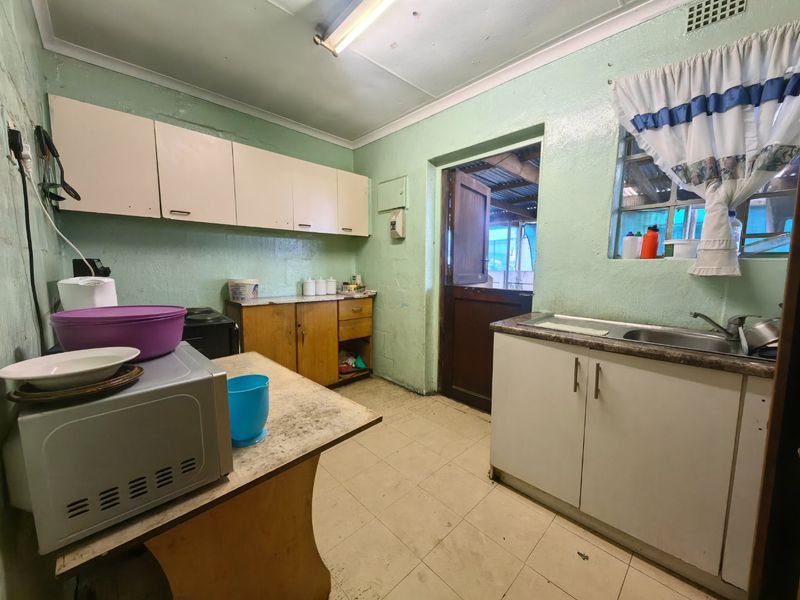 A functional kitchen featuring built-in cabinetry, laminate countertops, and a stainless steel sink, with direct access to an outdoor area via a stable door.