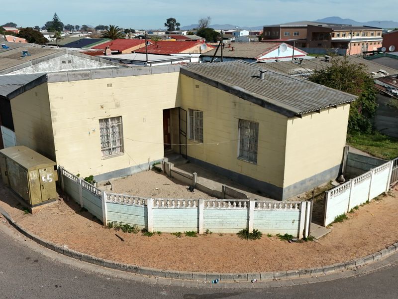 Aerial view of a detached single-story house featuring a corrugated metal roof, concrete block construction, and a perimeter boundary wall.