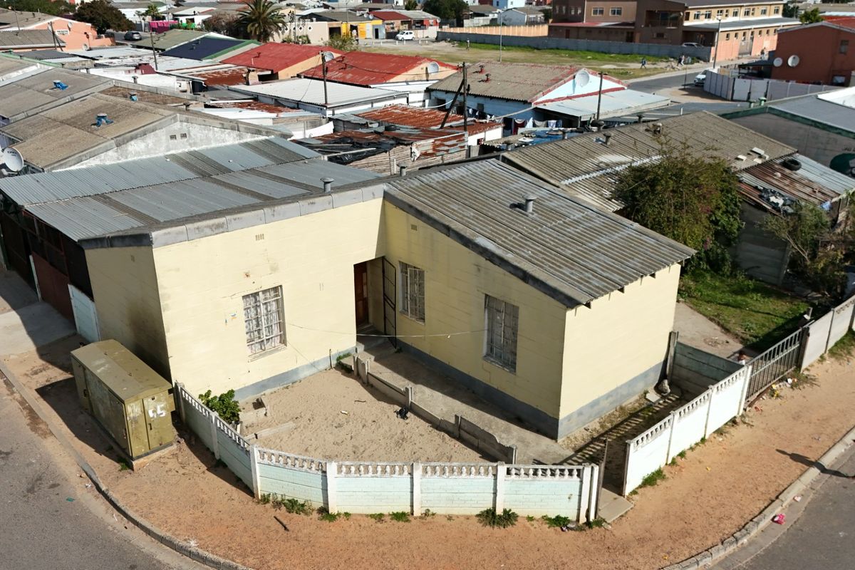 Aerial view of a single-story residential property featuring a corrugated metal roof and a fenced front yard area in a suburban setting.