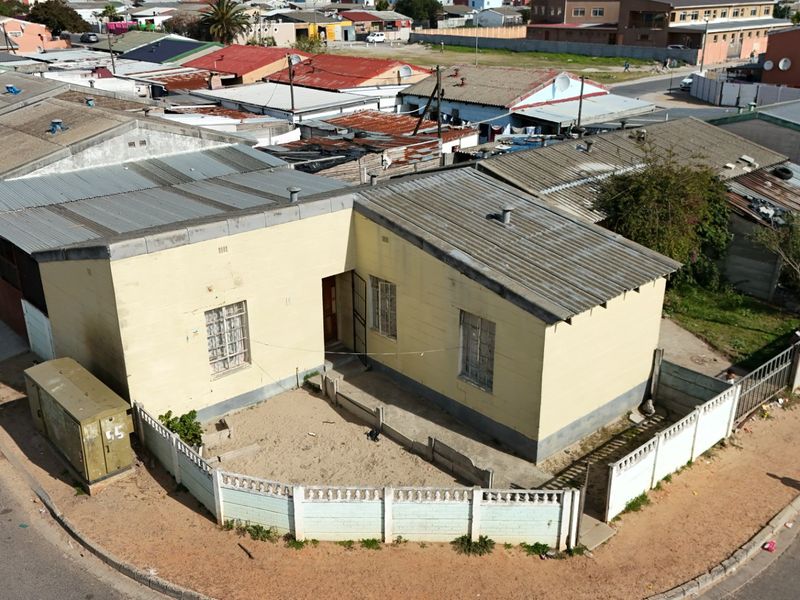 Aerial view of a single-story residential property featuring a corrugated metal roof and a fenced front yard area in a suburban setting.