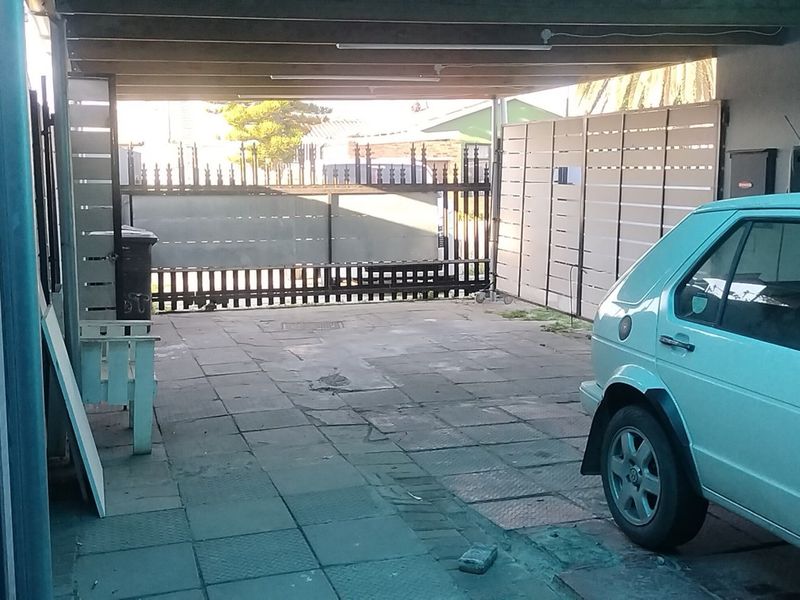 A covered carport area featuring paved flooring and a secure sliding gate entrance.