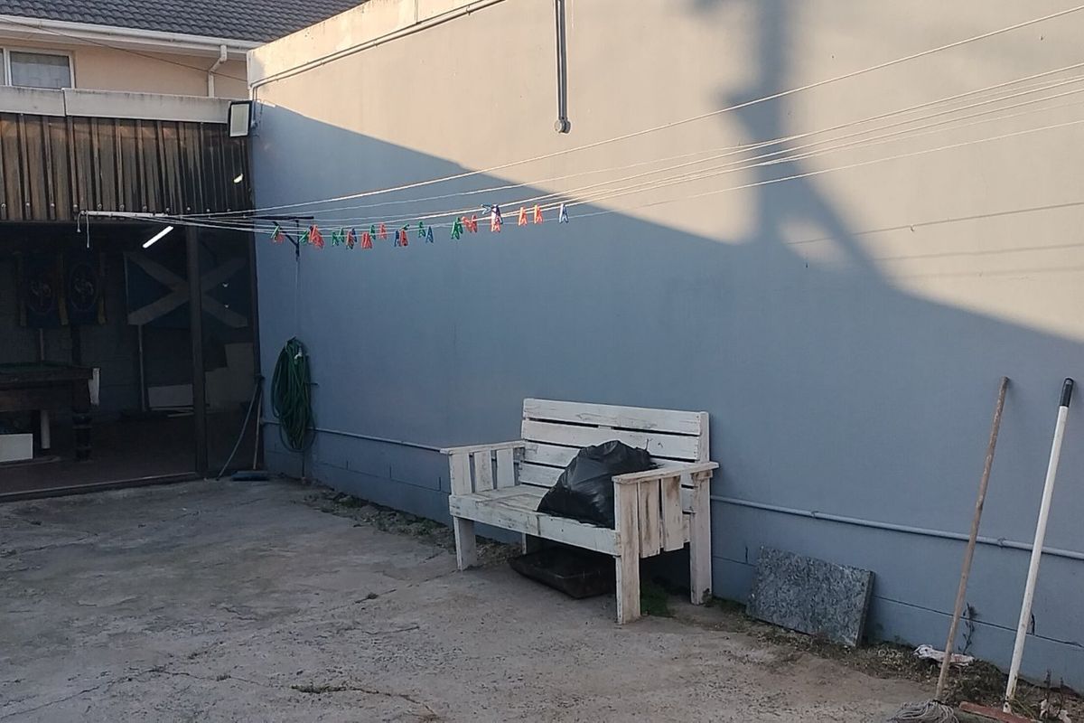 Rear exterior area featuring concrete paving, a covered utility space, and a wall-mounted clothesline, offering potential for outdoor improvement.