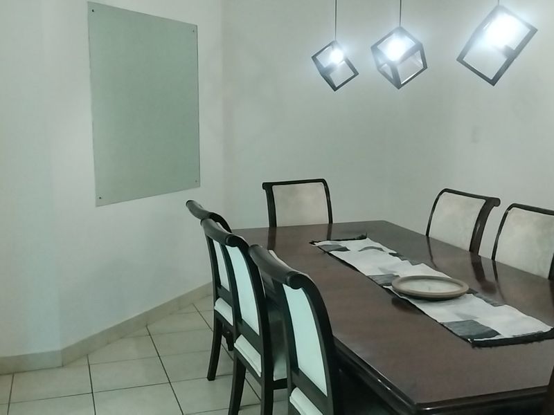 A dining area featuring ceramic floor tiles and modern pendant lighting, with an open-plan layout connecting to the kitchen space.