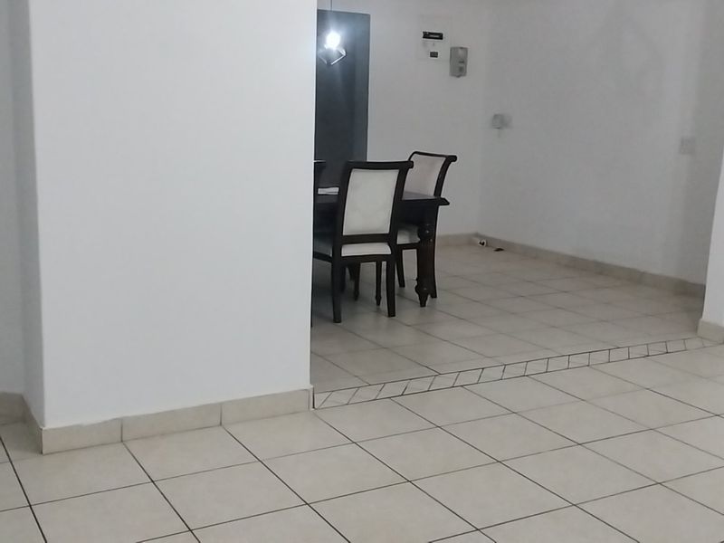 An open-plan living and dining area featuring neutral tiled flooring and a split-level layout, providing a blank canvas for interior design.