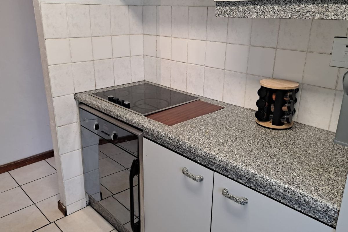 Compact kitchen area featuring a built-in oven, electric hob, granite-look laminate countertops, and tiled splashback finishes.