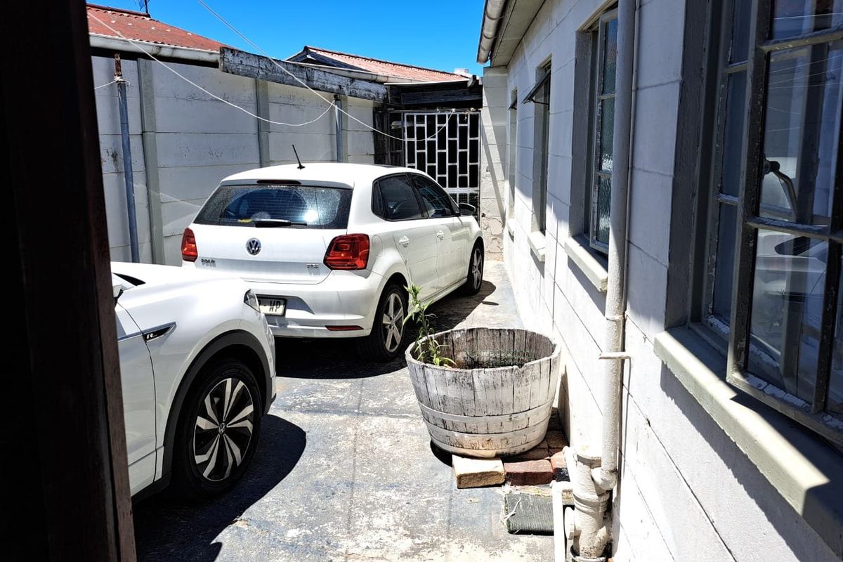 A narrow rear exterior side passage featuring concrete block walls, paved flooring, and security gate access.