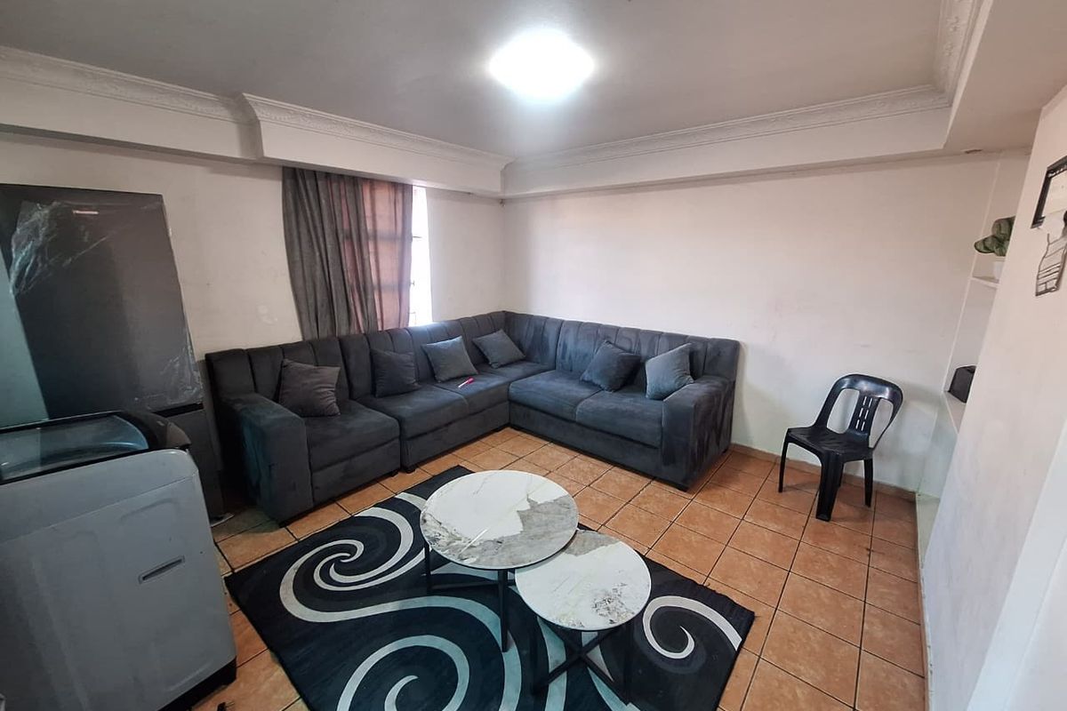 A living room featuring ceramic floor tiles and decorative ceiling cornicing, currently furnished with a large sectional sofa.