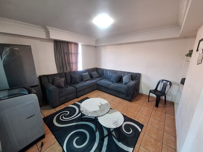 A living room featuring ceramic floor tiles and decorative ceiling cornicing, currently furnished with a large sectional sofa.