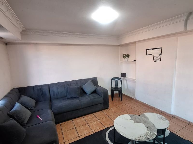 A living room featuring tiled flooring, built-in shelving, and decorative ceiling cornicing, requiring cosmetic updates to improve the overall aesthetic.
