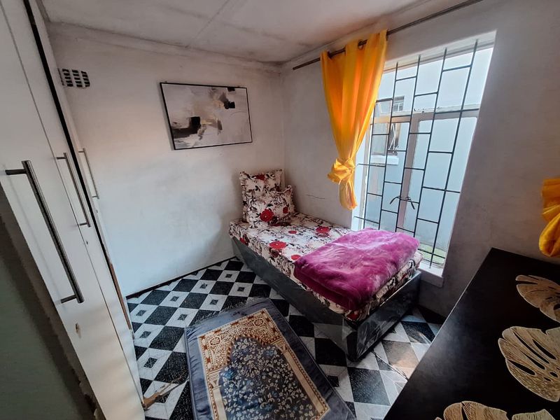 A compact bedroom featuring built-in wardrobe storage, patterned floor tiles, and a window fitted with security bars.
