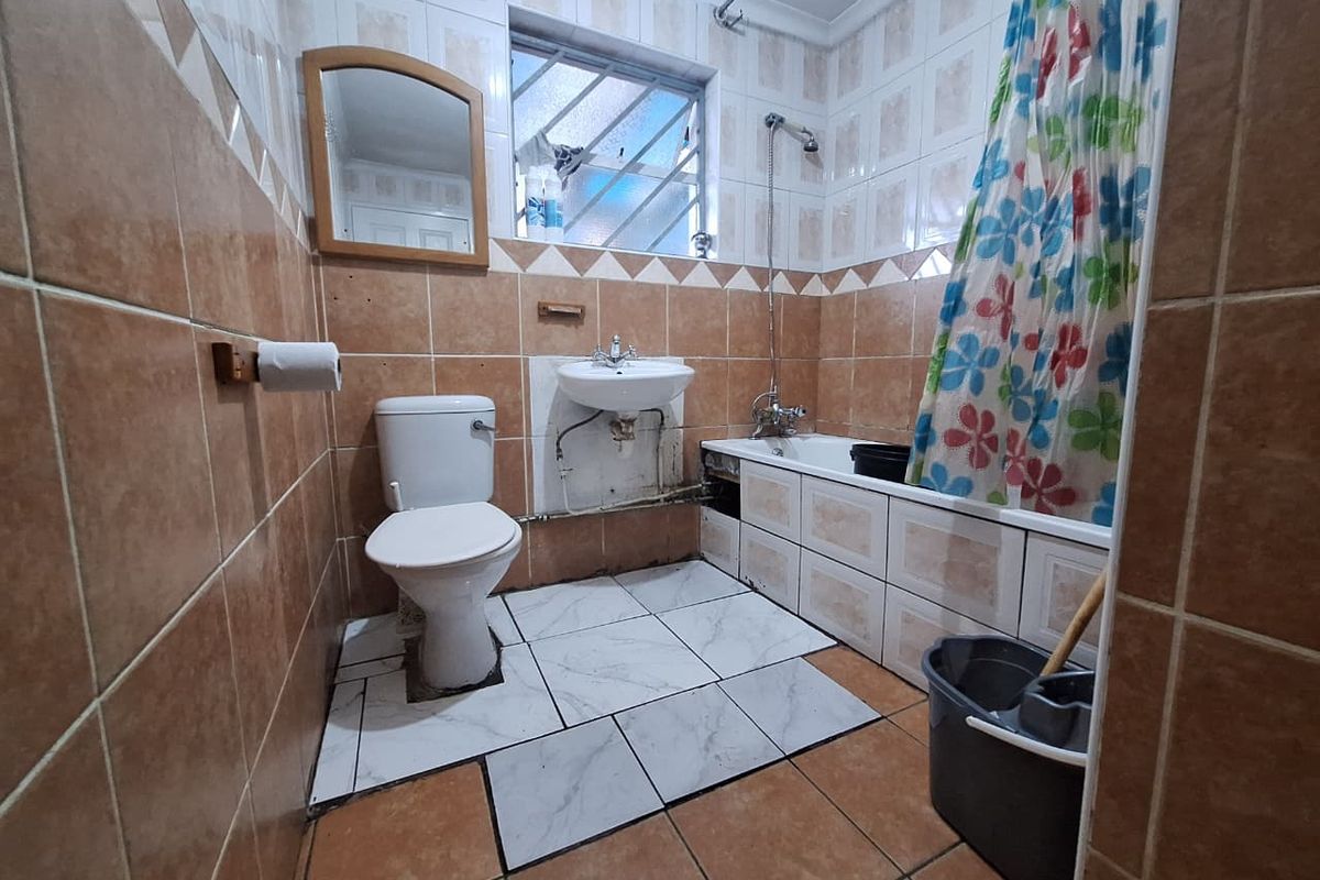 A functional bathroom featuring a bathtub with shower mixer, pedestal basin, and toilet, finished with tiled walls and flooring.