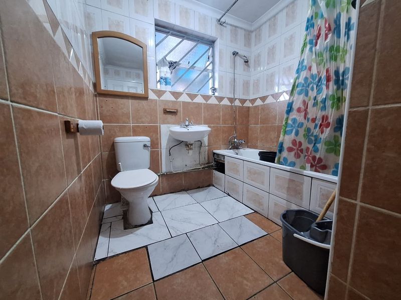 A functional bathroom featuring a bathtub with shower mixer, pedestal basin, and toilet, finished with tiled walls and flooring.