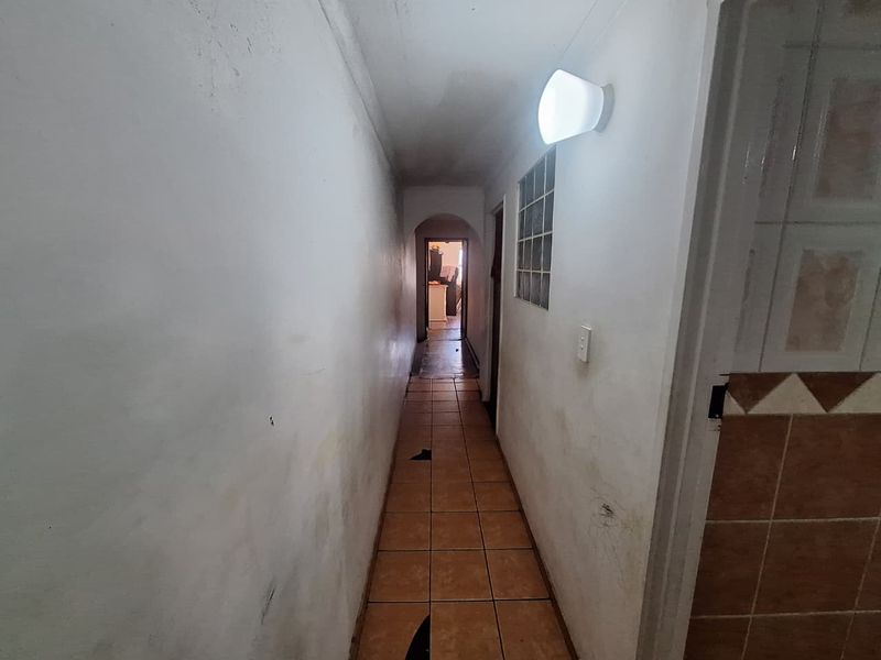 A narrow interior hallway featuring tiled flooring, a glass block window, and an arched transition to the adjacent living space.