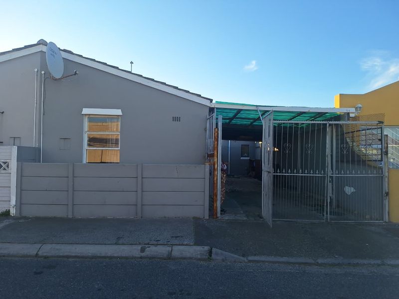 Front exterior view of the property featuring a precast concrete boundary wall, metal security gate, and a covered carport area.