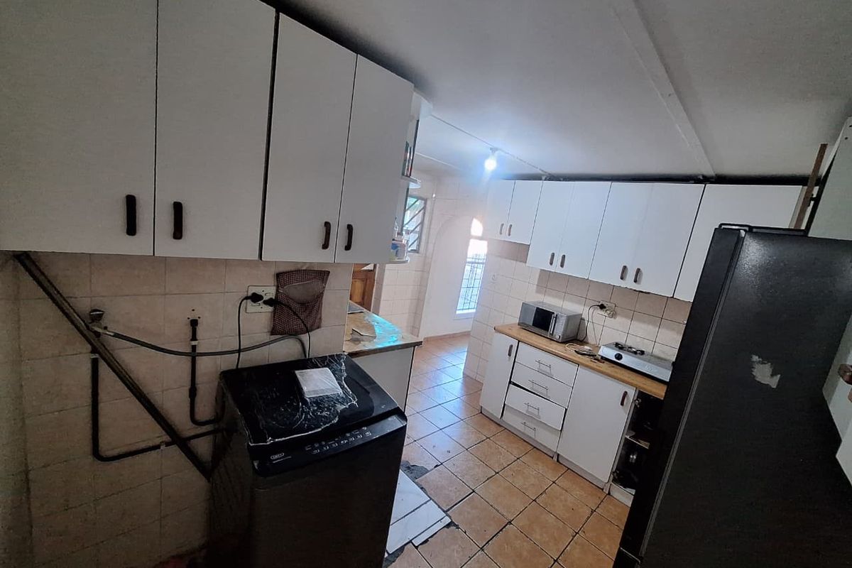 A functional kitchen featuring white cabinetry, tiled flooring, and a tiled backsplash, with visible plumbing and dated finishes requiring cosmetic updates.