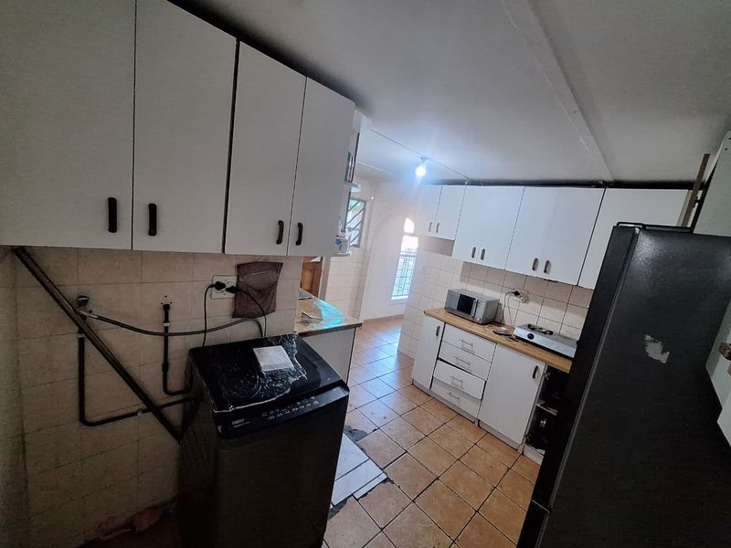 A functional kitchen featuring white cabinetry, tiled flooring, and a tiled backsplash, with visible plumbing and dated finishes requiring cosmetic updates.
