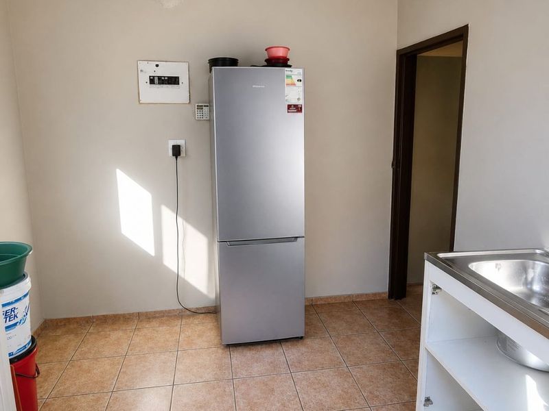 A functional laundry area featuring tiled flooring, a stainless steel sink, and exposed ceiling structure, providing a basic utility space.