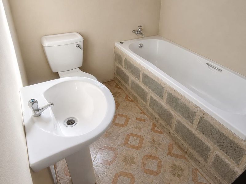 A functional bathroom featuring a pedestal basin, toilet, and bathtub with an unfinished concrete block surround, awaiting final tiling or finishing touches.
