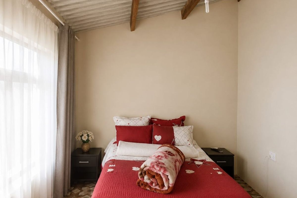 A bedroom featuring exposed timber rafters, a corrugated ceiling, and patterned floor tiles, offering a rustic aesthetic with potential for modernization.