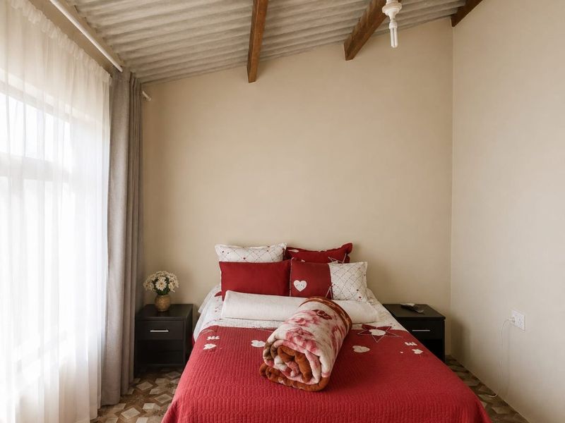 A bedroom featuring exposed timber rafters, a corrugated ceiling, and patterned floor tiles, offering a rustic aesthetic with potential for modernization.