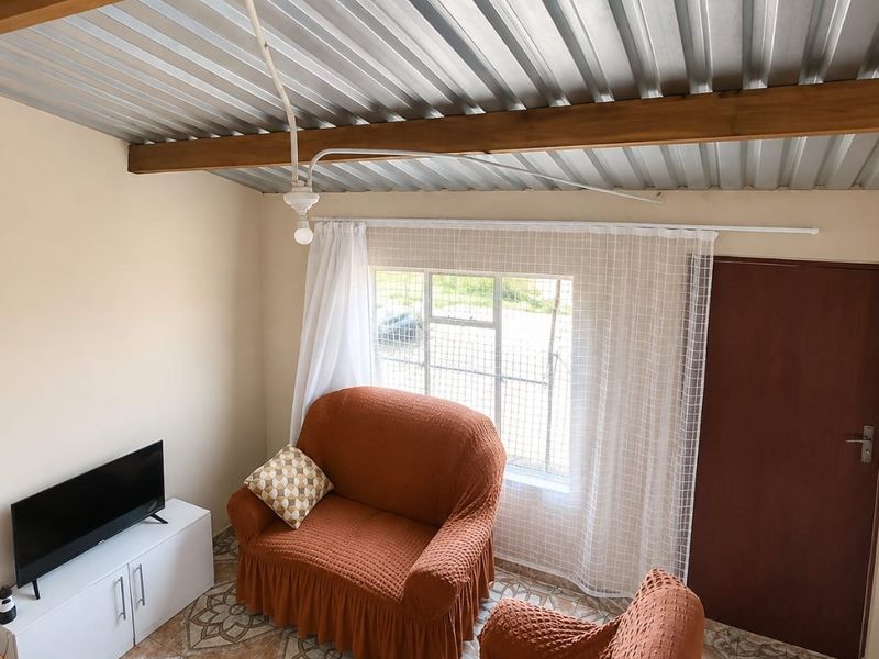 A living room featuring a corrugated metal ceiling with exposed timber beams and patterned tiled flooring.