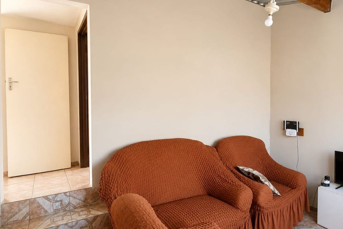 A living area featuring tiled flooring, decorative tiled steps, and an exposed timber beam with a corrugated metal ceiling.