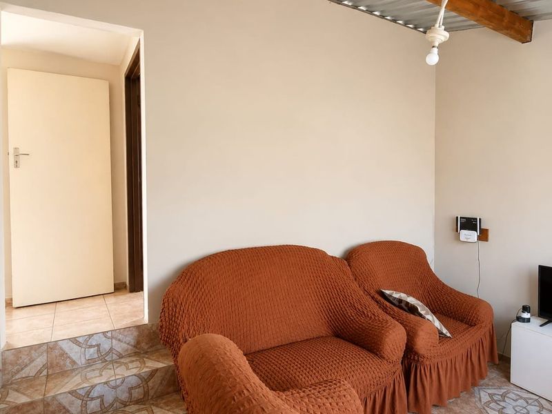 A living area featuring tiled flooring, decorative tiled steps, and an exposed timber beam with a corrugated metal ceiling.