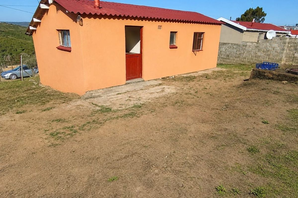 A detached outbuilding featuring a red corrugated metal roof and orange exterior walls, situated on a plot with a concrete apron and boundary wall.
