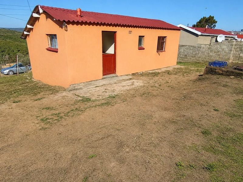 A detached outbuilding featuring a red corrugated metal roof and orange exterior walls, situated on a plot with a concrete apron and boundary wall.
