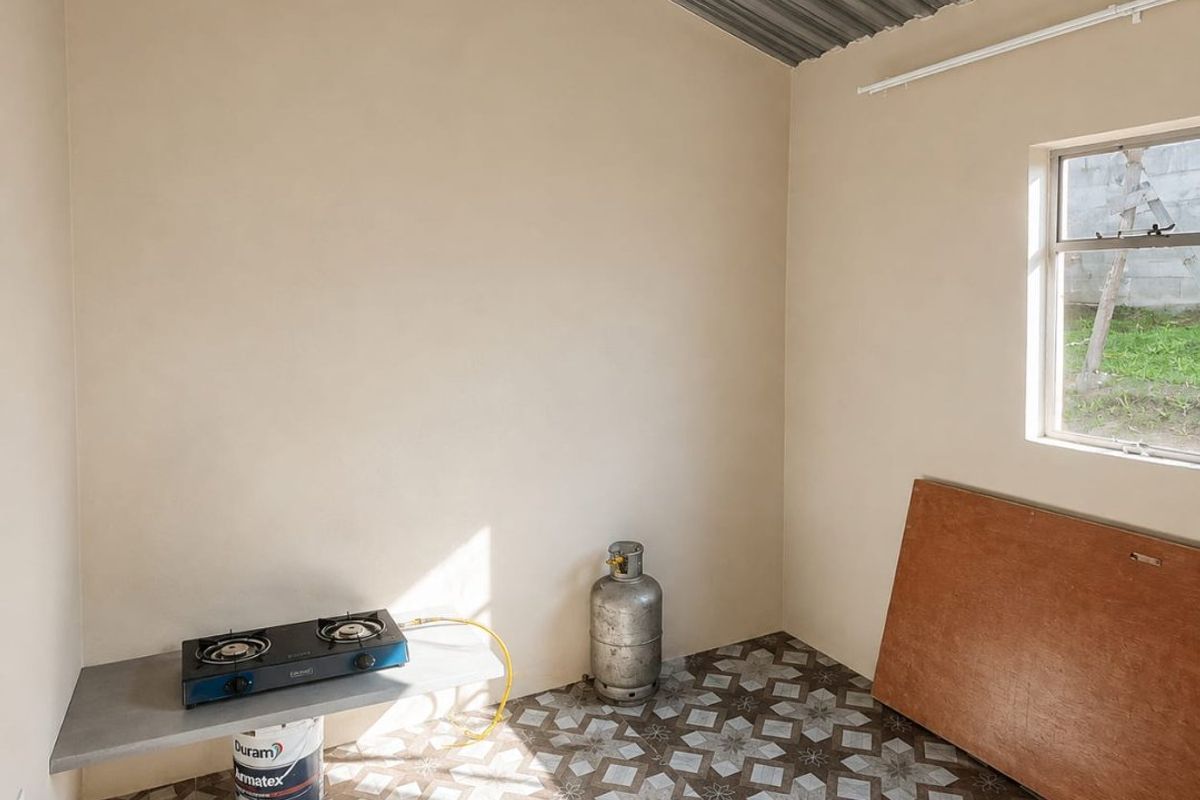 A basic, functional kitchen space featuring patterned floor tiles, a concrete prep shelf, and an exposed corrugated metal ceiling with timber beams.