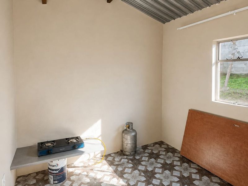 A basic, functional kitchen space featuring patterned floor tiles, a concrete prep shelf, and an exposed corrugated metal ceiling with timber beams.