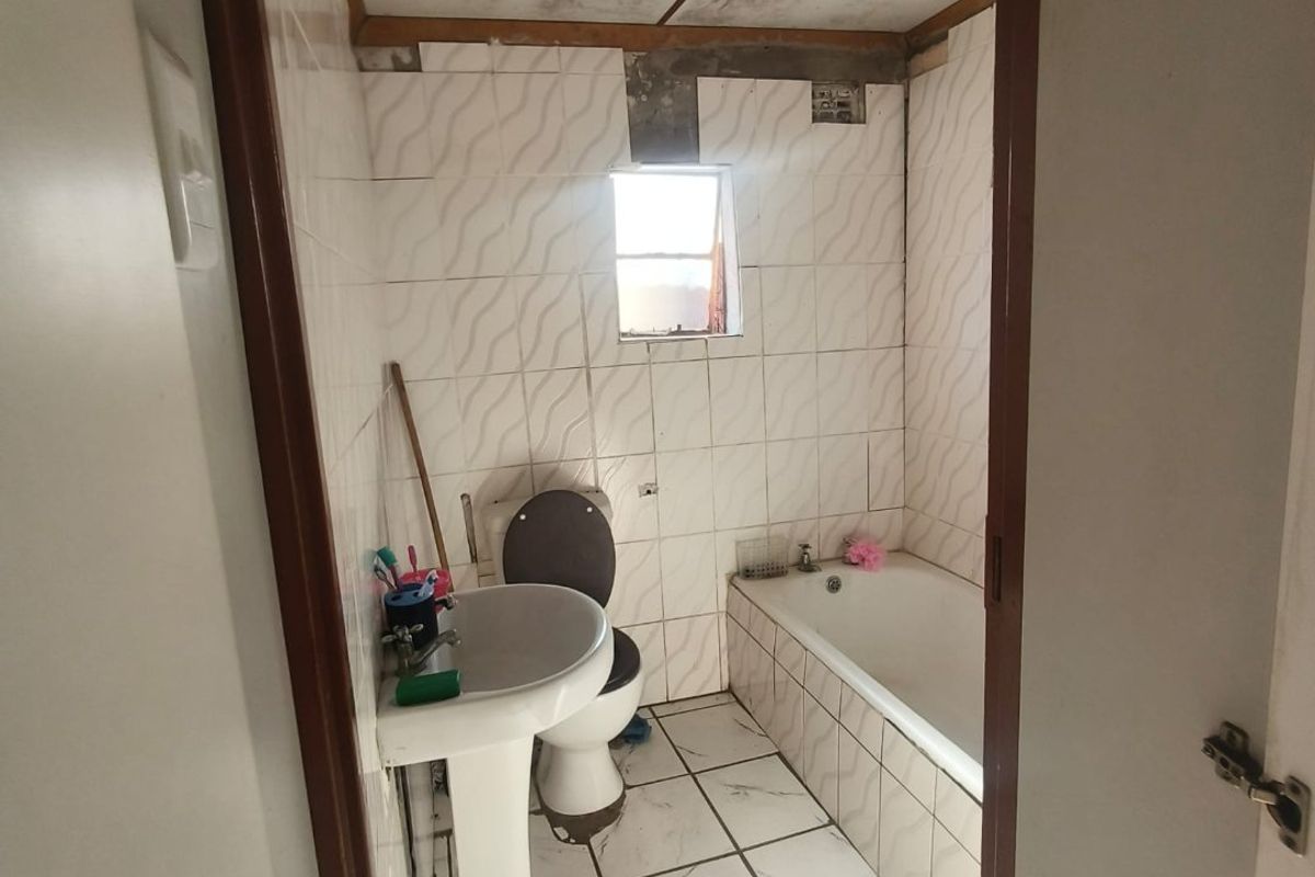 A compact bathroom featuring a pedestal basin, toilet, and bathtub with tiled finishes, currently requiring significant maintenance and cosmetic repairs to the ceiling and walls.