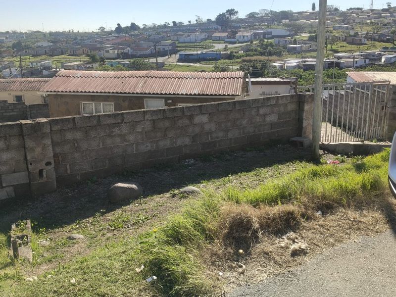 Street-level view showing the property boundary wall, metal gate, and surrounding neighbourhood landscape.