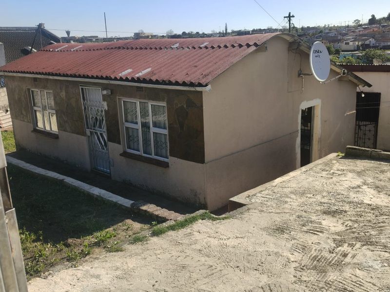 Front exterior view of a single-story house featuring a corrugated metal roof, stone cladding accents, and a concrete driveway.