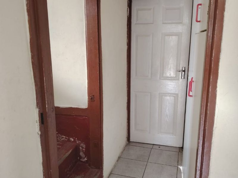 A functional hallway featuring tiled flooring and access to a staircase, showing signs of wear on the wooden door frames and stairs.