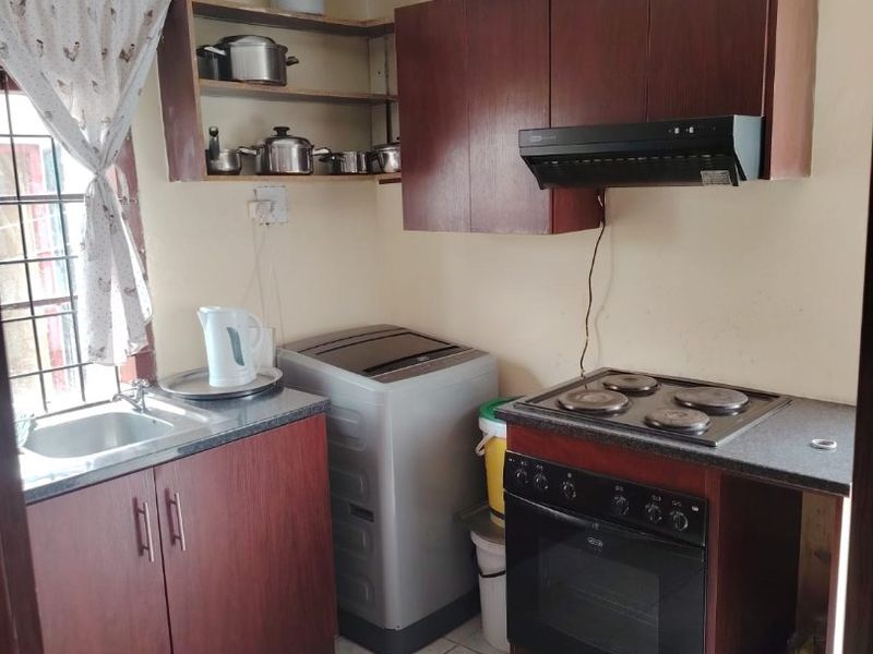 Compact kitchen featuring dark wood cabinetry, built-in oven with electric hob, extractor fan, and tiled flooring. Requires minor maintenance and cosmetic updates.