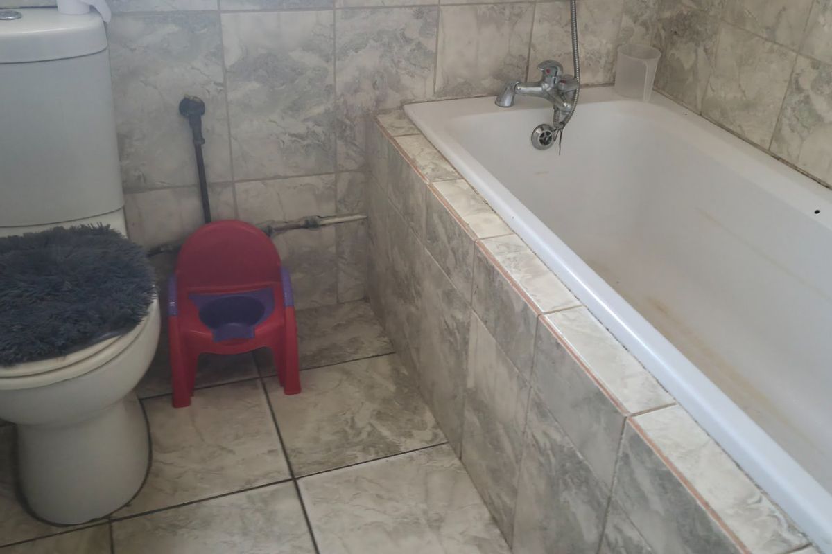 A functional bathroom featuring a bathtub and toilet with tiled finishes, showing signs of wear and visible plumbing.