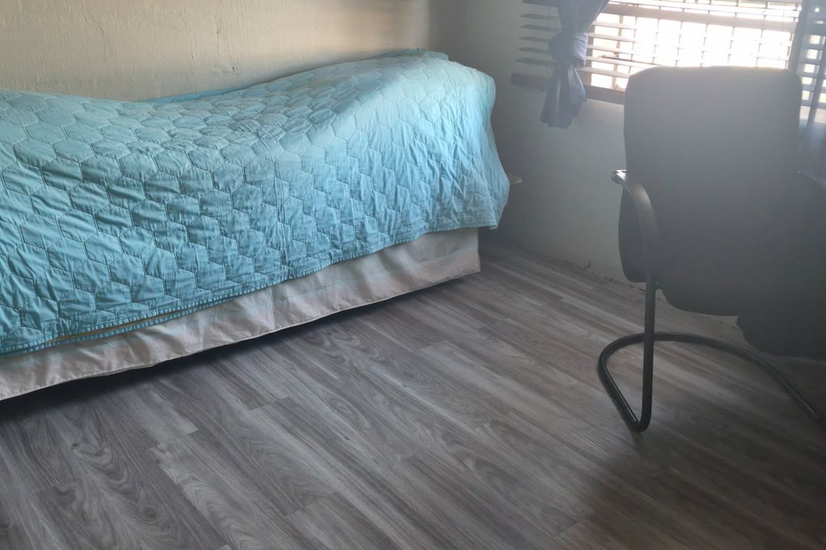A bedroom featuring modern grey laminate flooring and venetian blinds, providing a functional space with neutral wall finishes.
