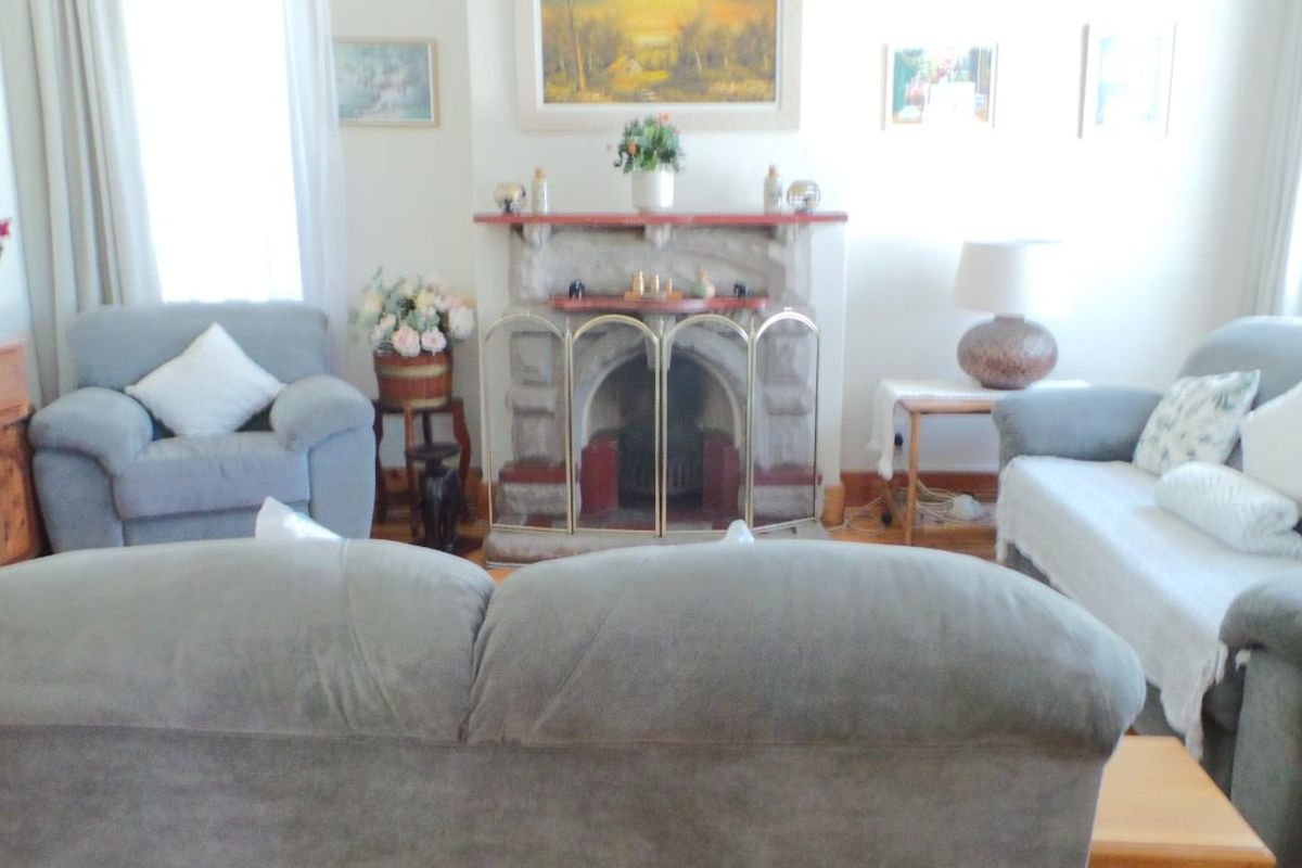 A cozy living room featuring a traditional stone fireplace with a timber mantelpiece and classic timber skirting boards.