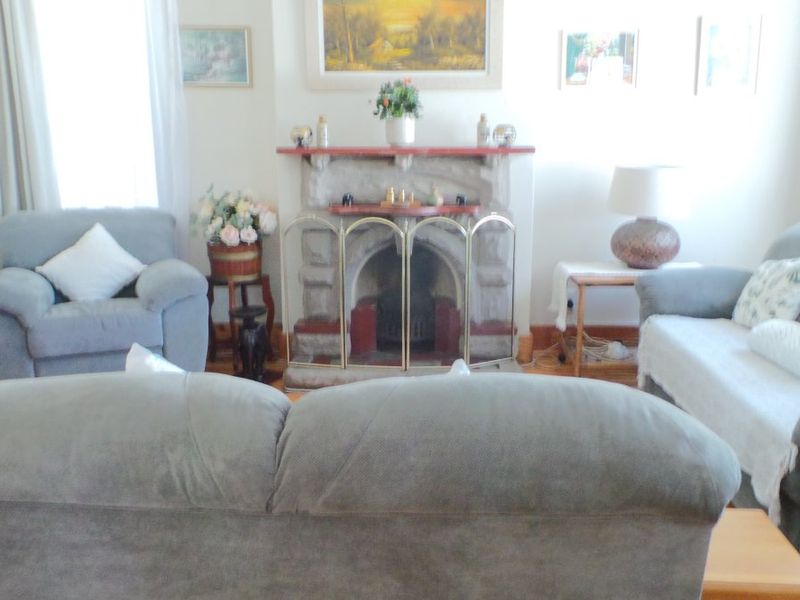 A cozy living room featuring a traditional stone fireplace with a timber mantelpiece and classic timber skirting boards.