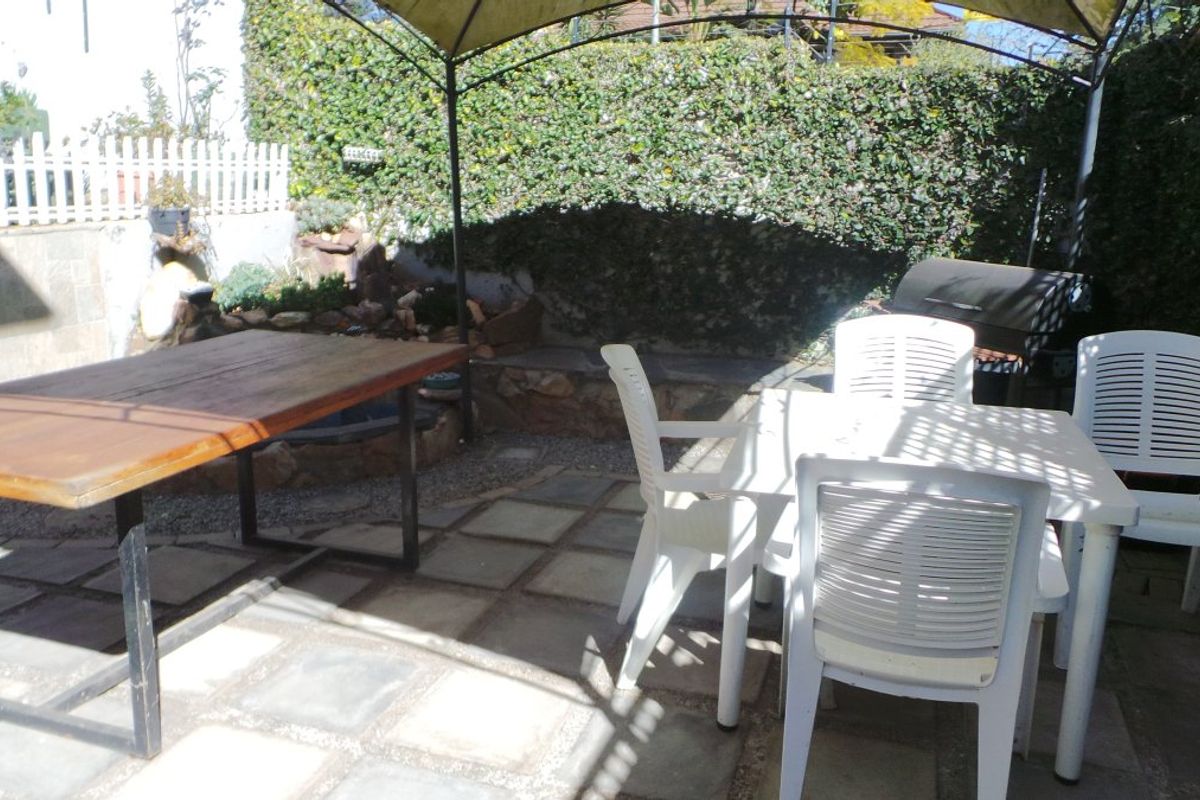 A paved outdoor patio area featuring a gazebo, retaining wall, and established garden boundary, providing a functional space for outdoor dining and relaxation.