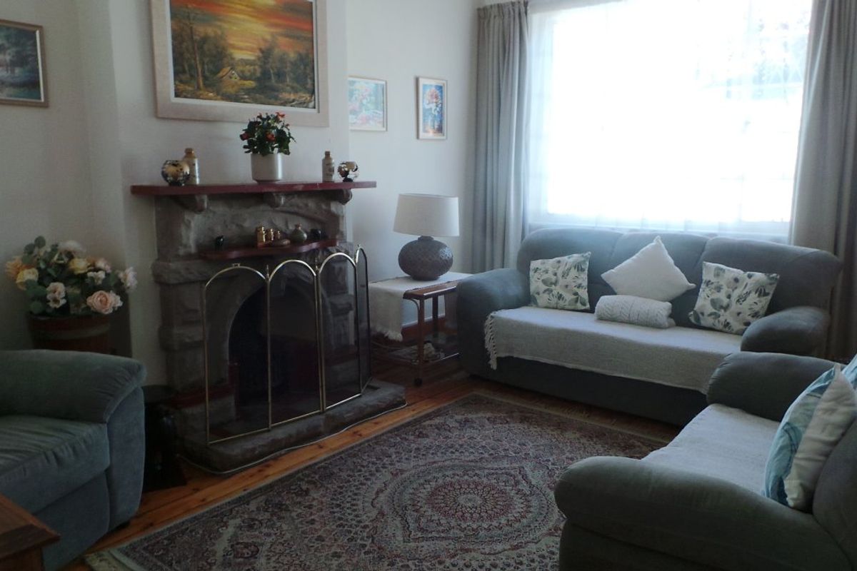 A cozy living room featuring a traditional stone fireplace with a timber mantelpiece and polished timber flooring.