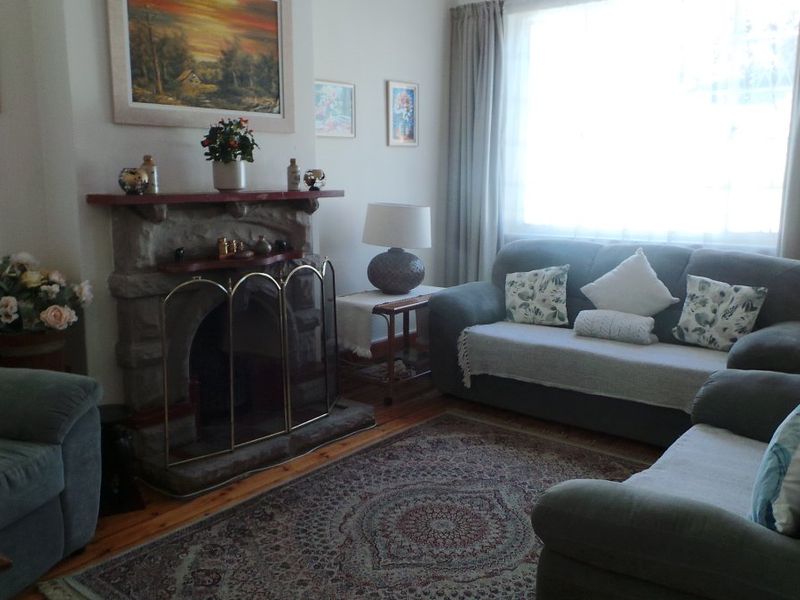 A cozy living room featuring a traditional stone fireplace with a timber mantelpiece and polished timber flooring.