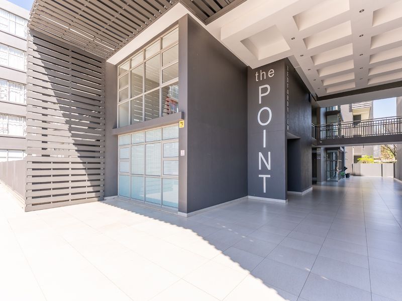Modern apartment building entrance featuring a covered walkway, tiled flooring, and contemporary architectural design with large glass windows and metal screening.
