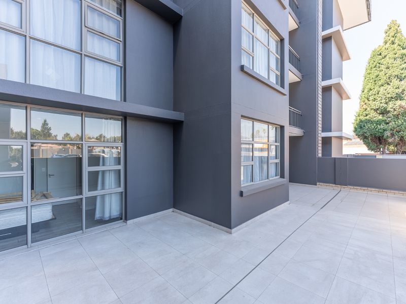 A spacious, modern ground-floor patio area featuring large glass sliding doors and clean tiled flooring, offering a seamless transition to the apartment interior.