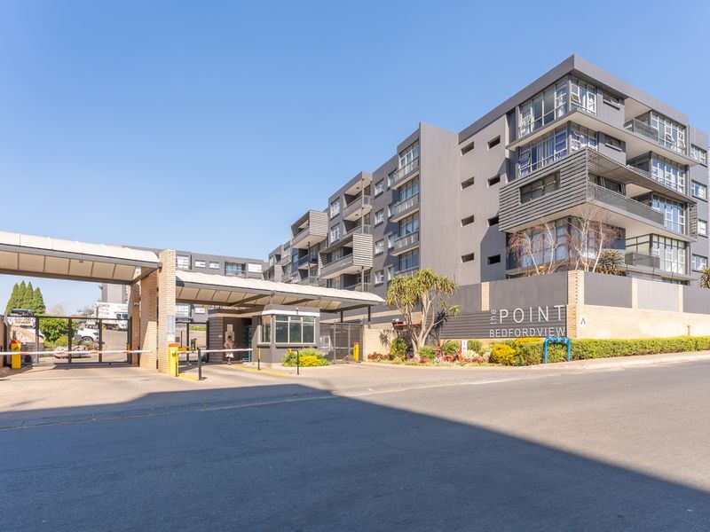 Exterior view of The Point Bedfordview apartment complex, featuring a secure gated entrance, guard house, and modern multi-story residential building architecture.