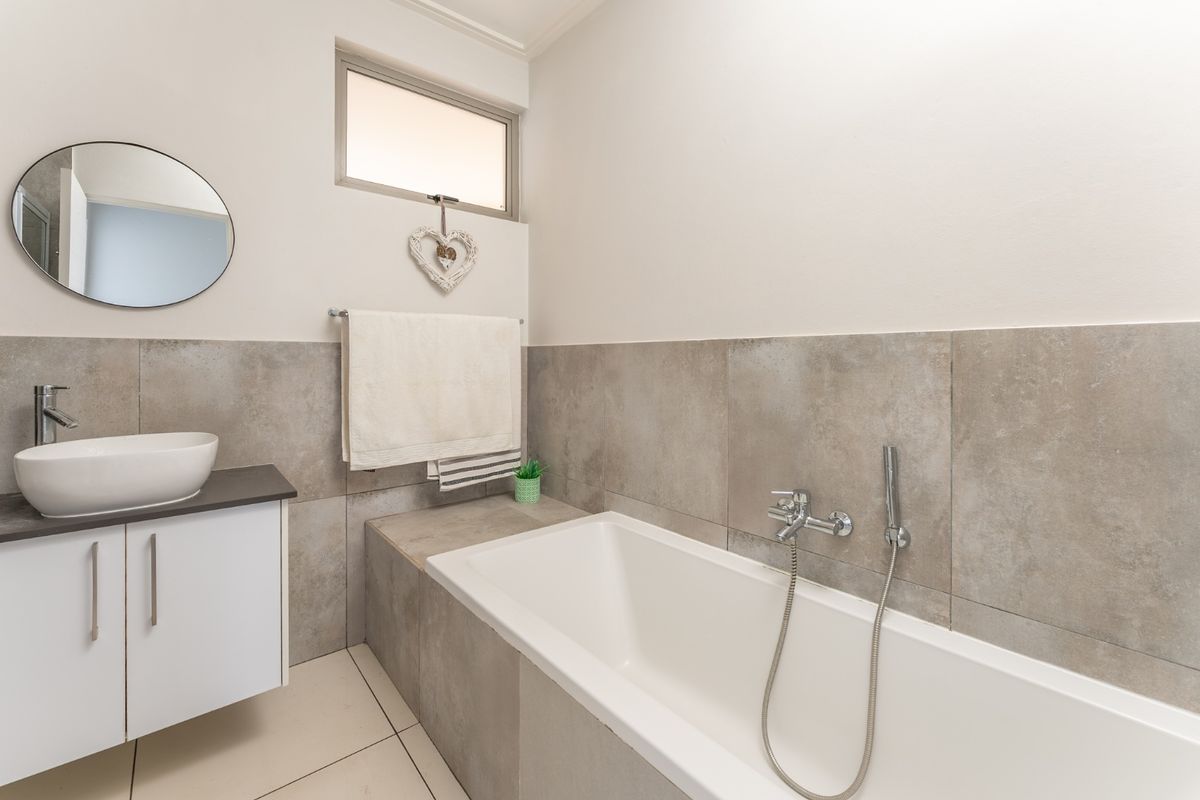 Modern bathroom featuring a vessel sink on a vanity cabinet, a built-in bathtub with a handheld shower mixer, and neutral grey wall tiling.
