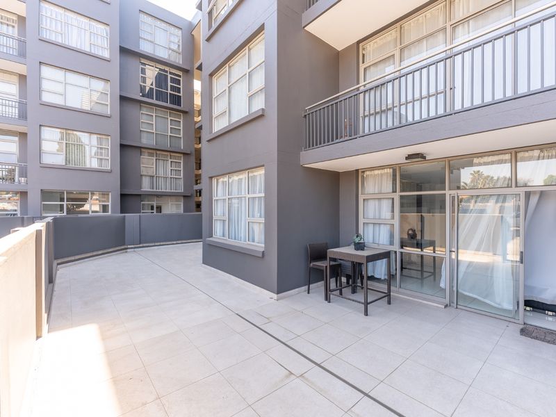 A spacious, modern apartment balcony featuring tiled flooring, metal railings, and large glass sliding doors providing access to the interior living space.