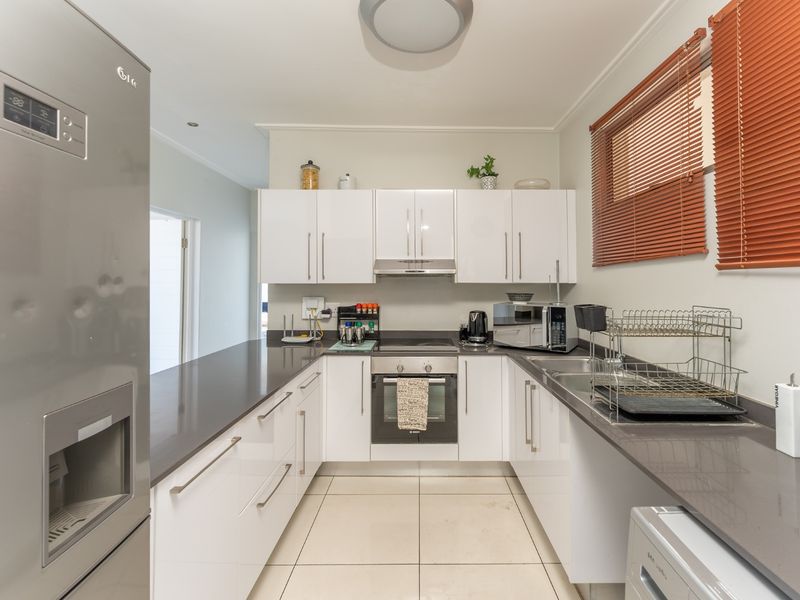 Modern kitchen featuring white gloss cabinetry, stone countertops, built-in oven, electric hob, extractor fan, and a stainless steel double sink.