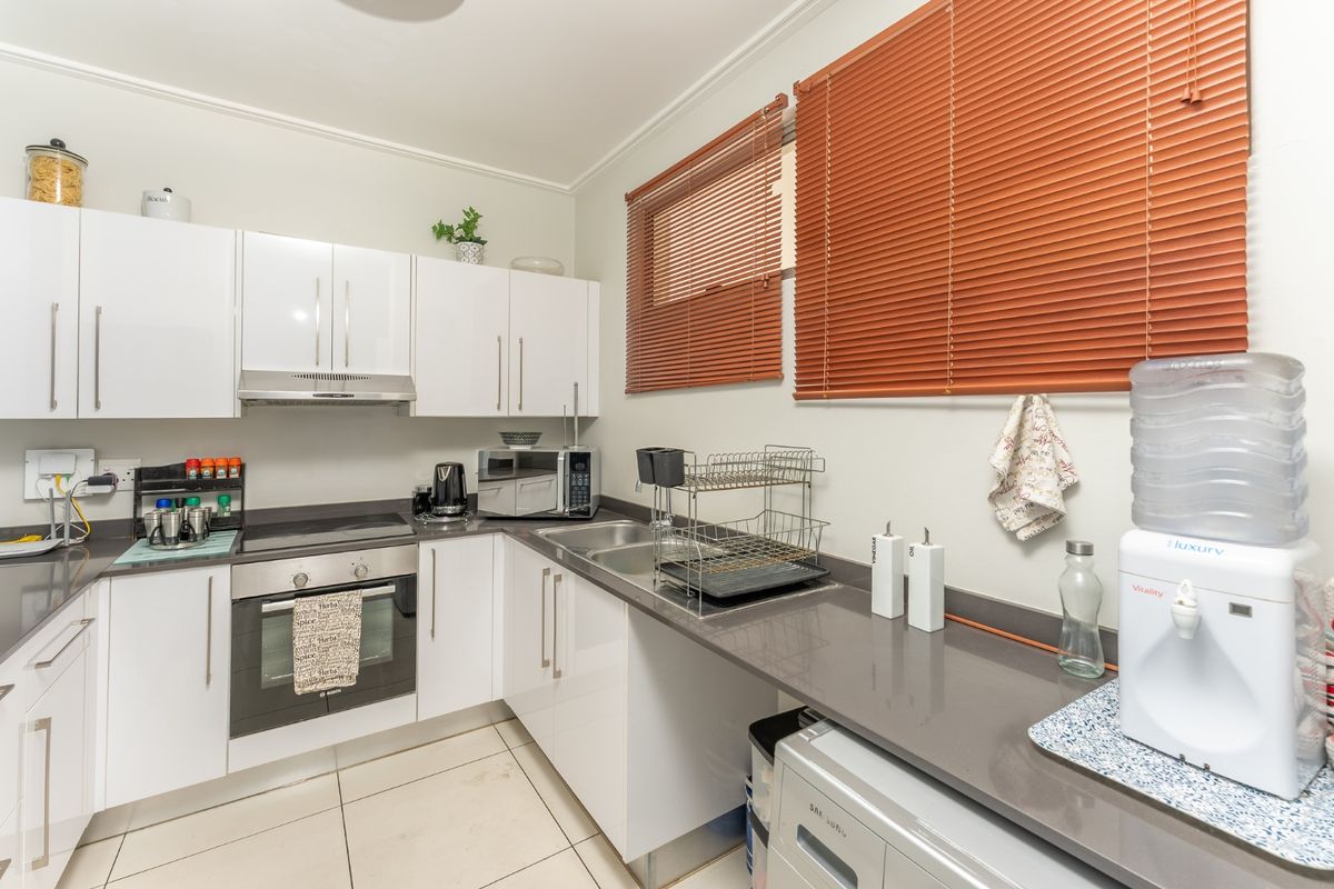 A functional kitchen featuring white gloss cabinetry, stone countertops, built-in oven, electric hob, and a stainless steel double sink with tiled flooring.